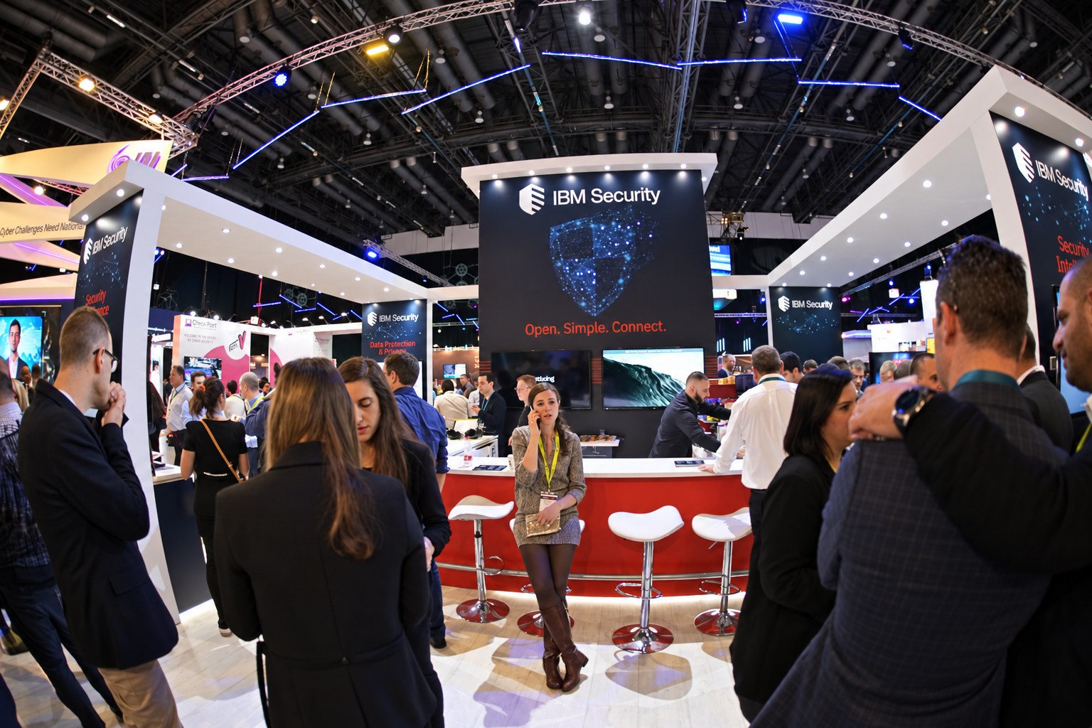 Visitors gather around a red counter beneath IBM Security signs, white illuminated booth frames and blue ceiling lights.